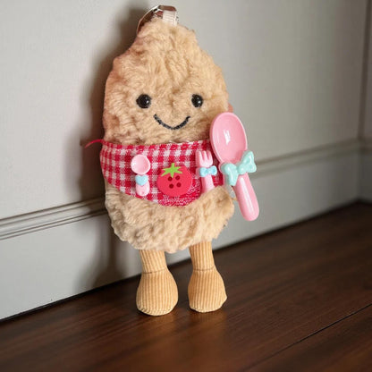 Jellycat peanut keychain wearing a red gingham apron decorated with pink spoon, fork, and tomato badge. Cute chef style doll outfit. Doll not included.