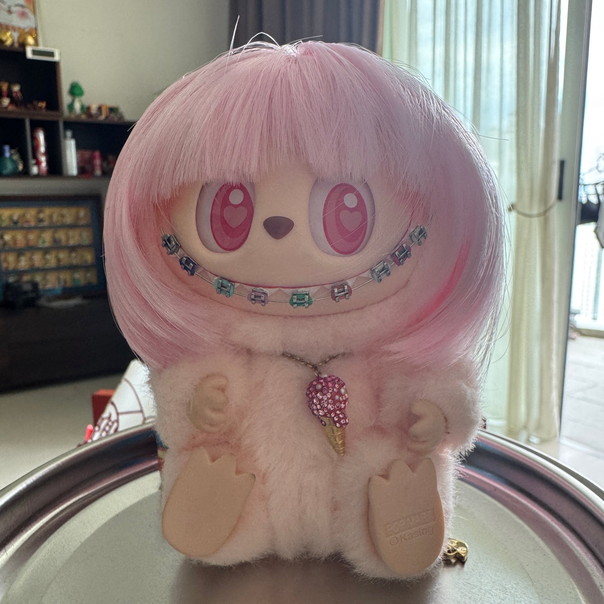Labubu doll with pink wig and white fur outfit wearing colorful handmade doll braces, posed on a metallic reflective surface. Example of installed cosplay accessory. Doll and outfit not included.