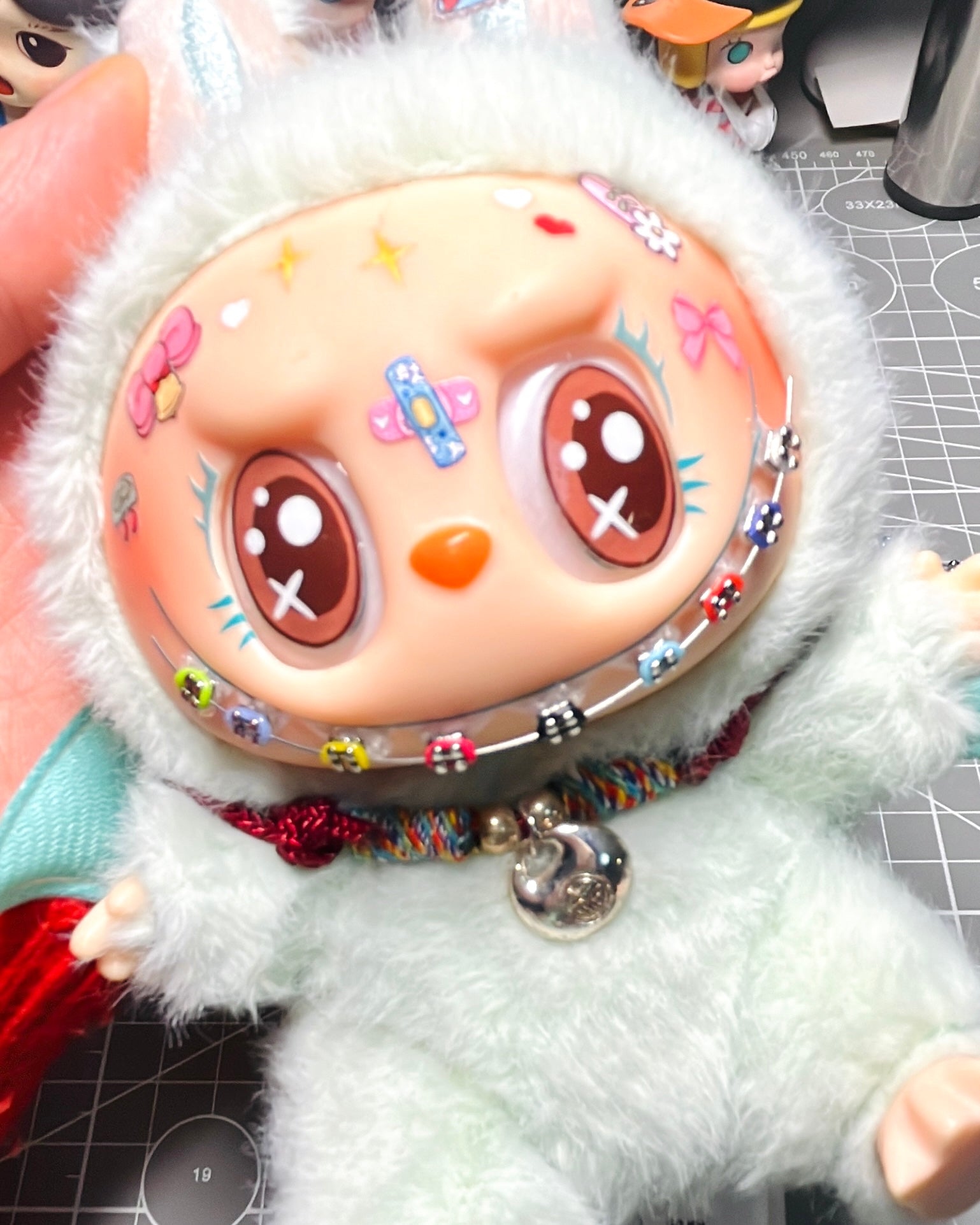 Close-up of Labubu doll with colorful braces and face stickers, styled on a craft cutting mat