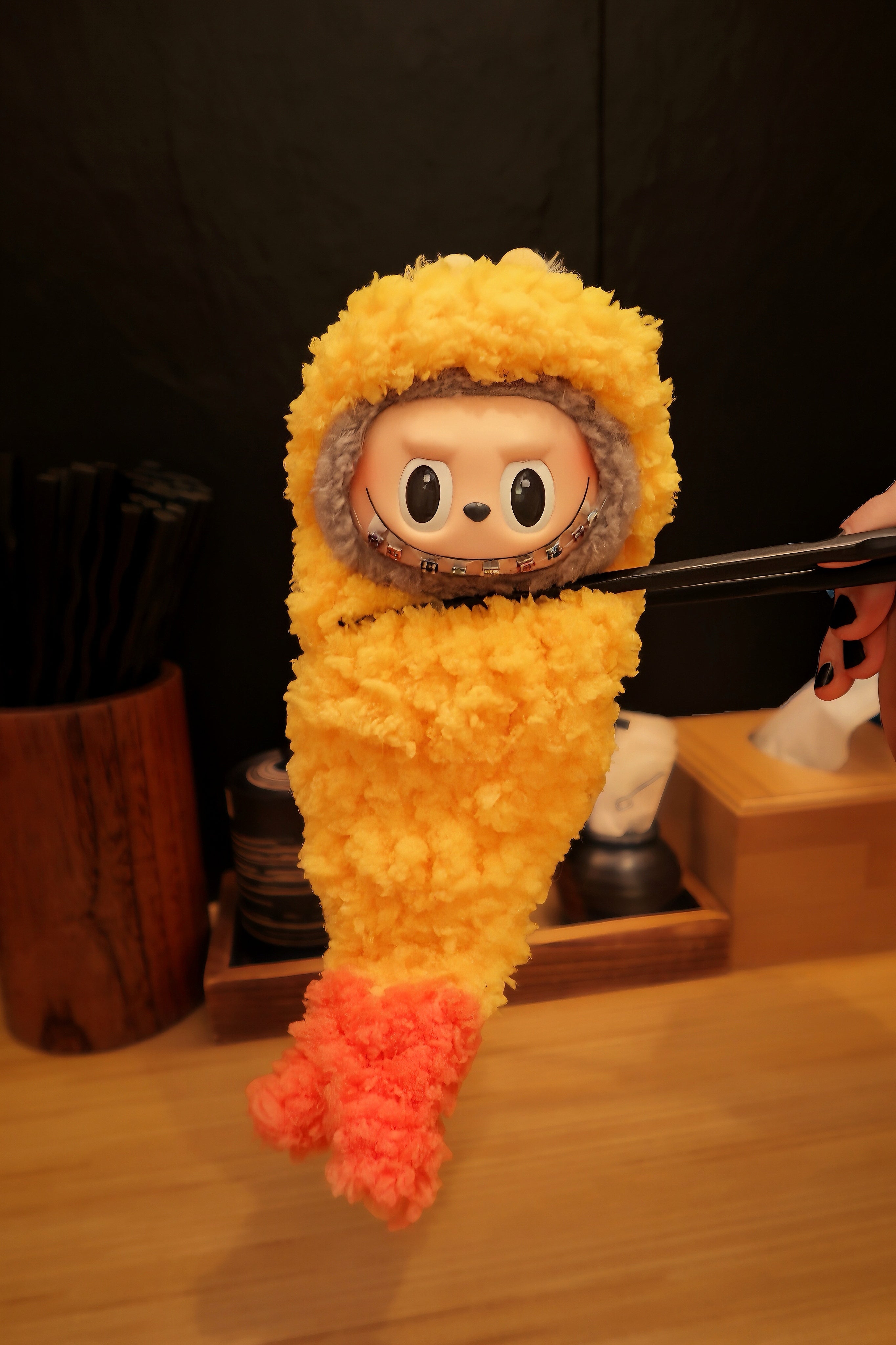 Labubu plush wearing a fried tempura outfit held with chopsticks against a dark background