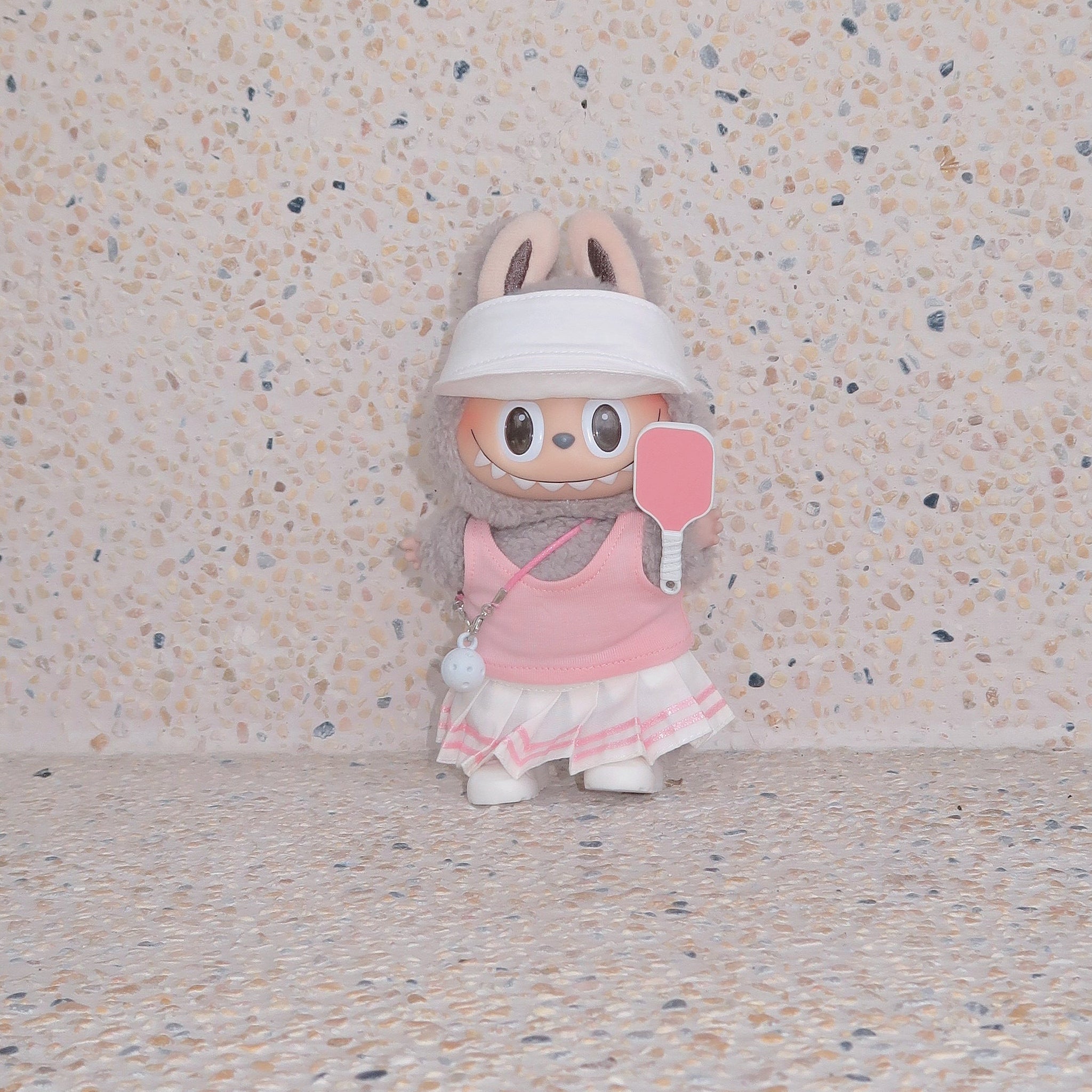 Labubu doll in pink pickleball outfit with visor and paddle, standing against terrazzo beige background, Popanion handmade doll fashion